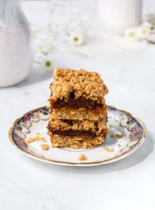 Two squares of date square stacked on a plate. Coffee mug a creamer cup in the background with white flowers.