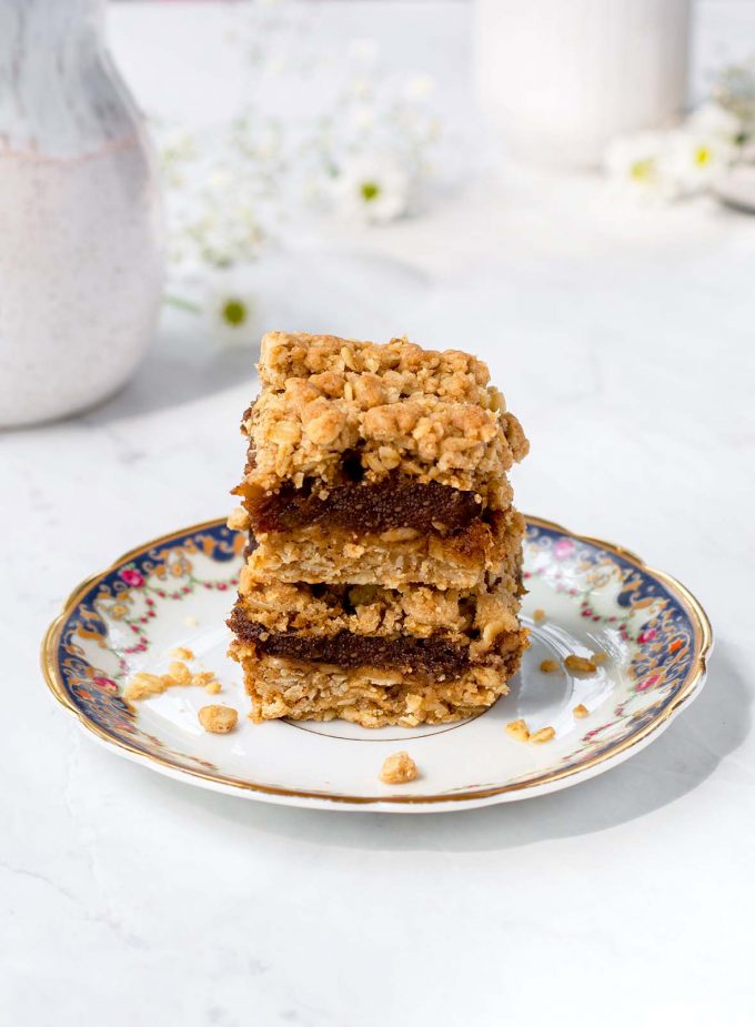 Two squares of date square stacked on a plate. Coffee mug a creamer cup in the background with white flowers.