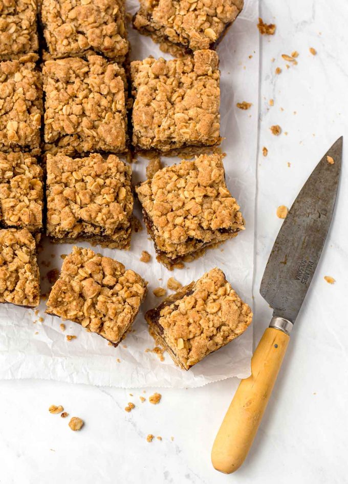 overhead shot of date squares cut into square pieces on a piece of white parchment. Knife to the right side with a wooden handle.