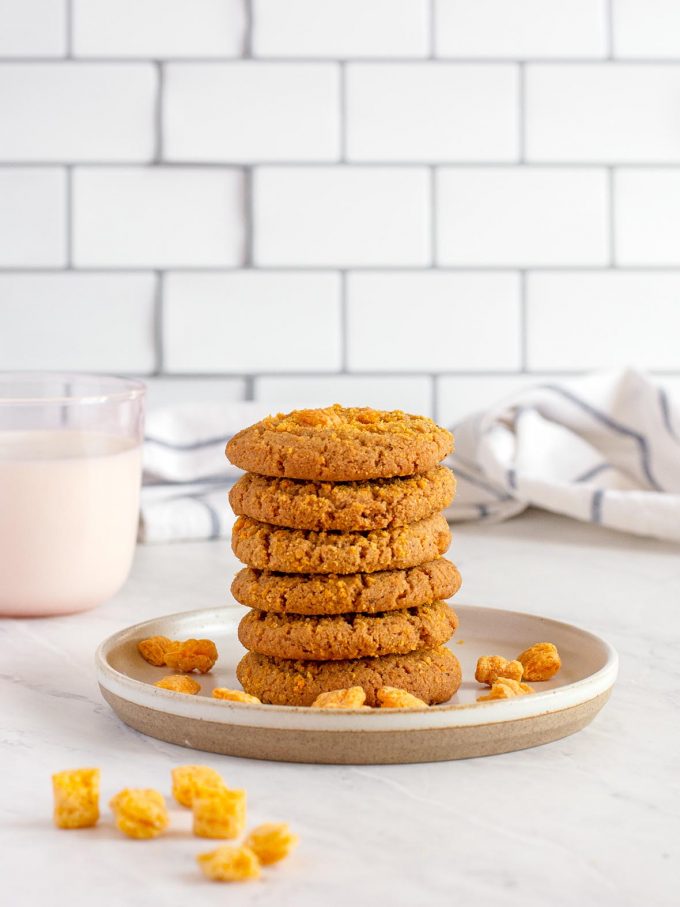 six golden Cap'n Crunch Cookies stacked into a tower on a plate. Cap'n Crunch cereal nuggets scattered on the plate.