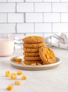 Six Cap'n Crunch Cookies stacked into a tower, with one leaning up against them. Cap'n Crunch cereal nuggets scattered no on the plate.
