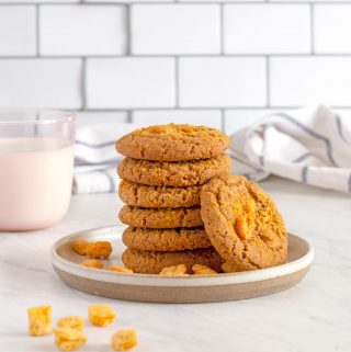 Six Cap'n Crunch Cookies stacked into a tower, with one leaning up against them. Cap'n Crunch cereal nuggets scattered no on the plate.