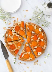 Round Tart with apricot halves in an almond filling, with sliced almonds scattered on top. Small white daisies scattered on top as well.