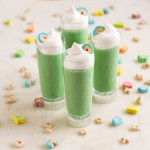 Four tall shot glasses filled with green pudding and topped with whipped cream and rainbows marshmallows