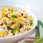 Large white bowl sitting on a red-striped napkin, filled with rotini pasta, bacon, and green onions