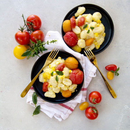 overhead shot of Sweet Corn and Roasted Tomato Gnocchi on two black plates.