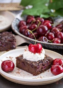 Brownie on a small plate, topped with whipped cream and a large cherry