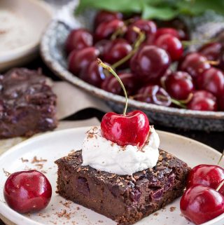 Brownie on a small plate, topped with whipped cream and a large cherry