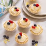 Seven mini lemon cream cheese tarts on a marble counter top.