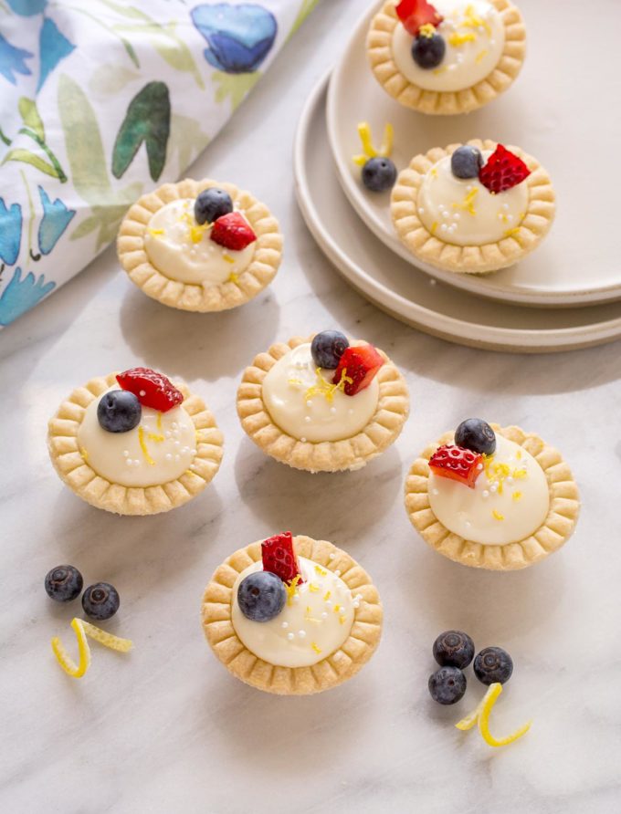 Seven mini lemon cream cheese tarts on a marble counter top.