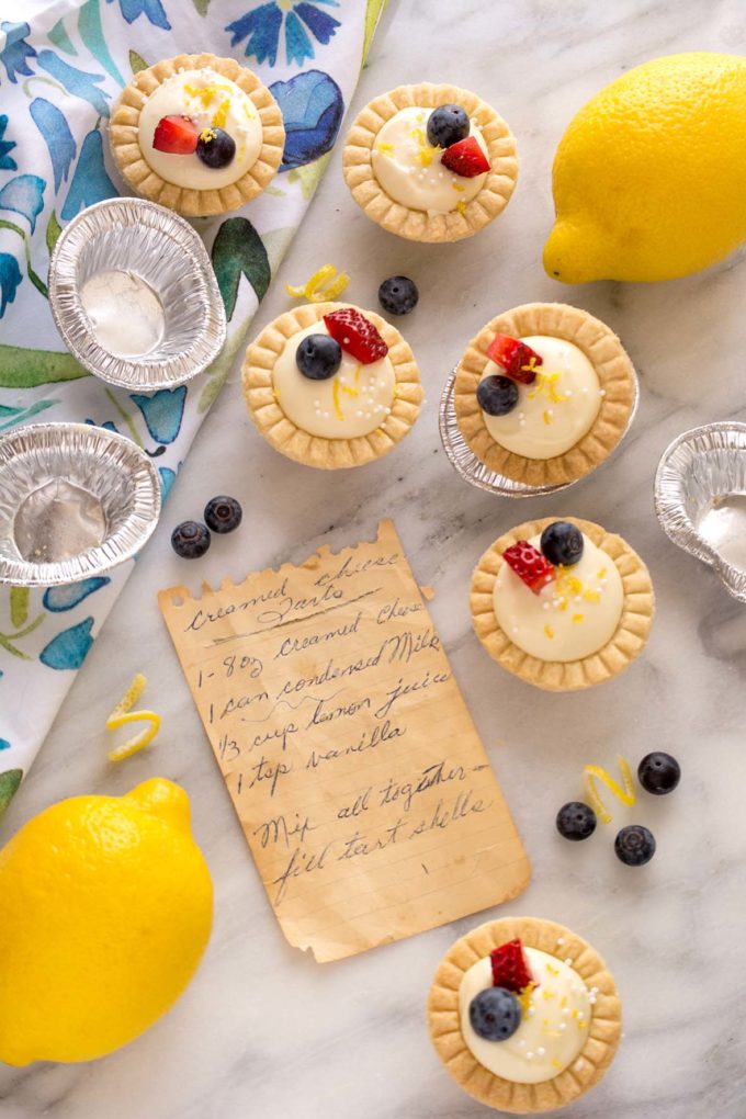 Six mini lemon cream cheese tarts sitting beside Nana's handwritten recipe on yellowed notebook paper.