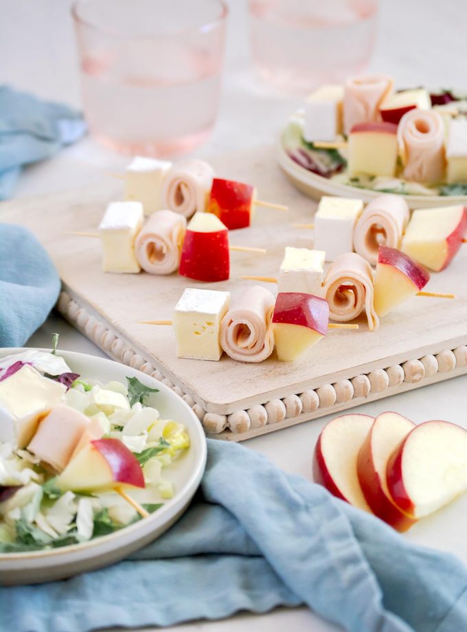 cubes of brie cheese, gala apples and deli turkey on cocktail skewers served on top of a green kale salad