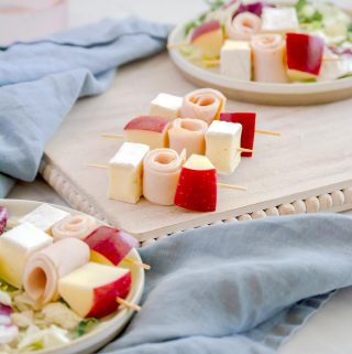 cubes of brie cheese, gala apples and deli turkey on cocktail skewers served on top of a green kale salad