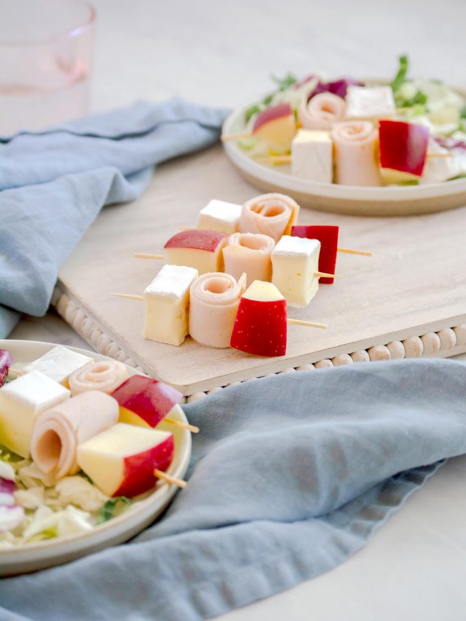 cubes of brie cheese, gala apples and deli turkey on cocktail skewers served on top of a green kale salad