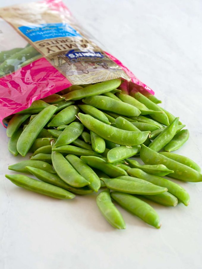 Open bag of snap peas, spilling out across the table top