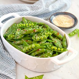 Small white serving dish filled with snap peas, sesame seeds in a small bowl in the background