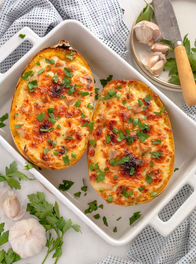 White casserole dish with two squash halves, filled with turkey, shredded squash and cheese