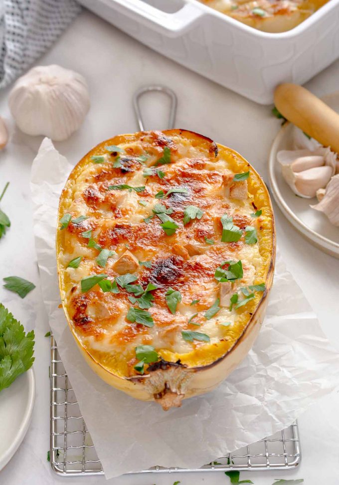 One spaghetti squash half on top of parchment and a cooling rack, filled with turkey, shredded squash and browned, melty cheese