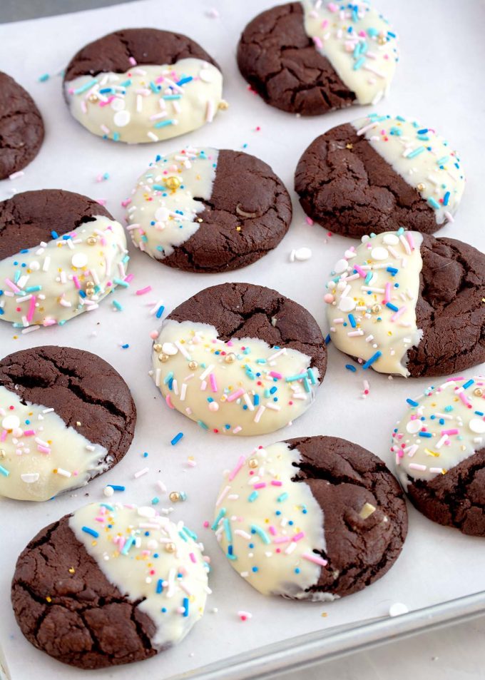 Cookie sheet with twelve chocolate cookies and each cookie is half dipped in white chocolate with sprinkles