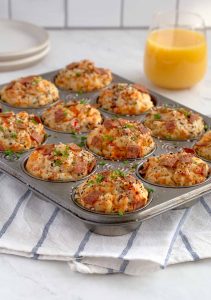 twelve muffins inside a muffin tin with glass of orange juice in the background