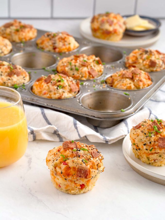 one muffin sitting on counter, one muffin on a plate and ten muffins in a muffin tin in the background