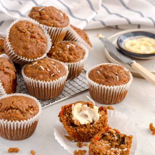 bran muffin cut in half with butter spread on one side. Several other muffins stacked on a cooling rack in the background