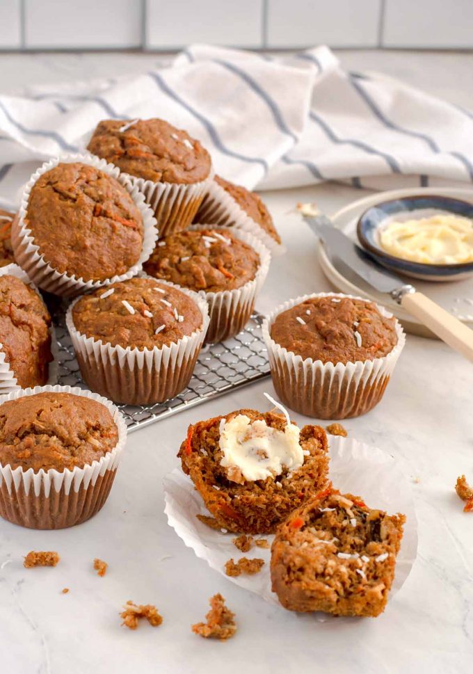 bran muffin cut in half with butter spread on one side. Several other muffins stacked on a cooling rack in the background