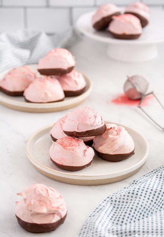 Round pink meringue cookies dipped in chocolate and placed on two small plates