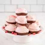 round pink meringue cookies dipped in chocolate and stacked on a small white cake pedestal.