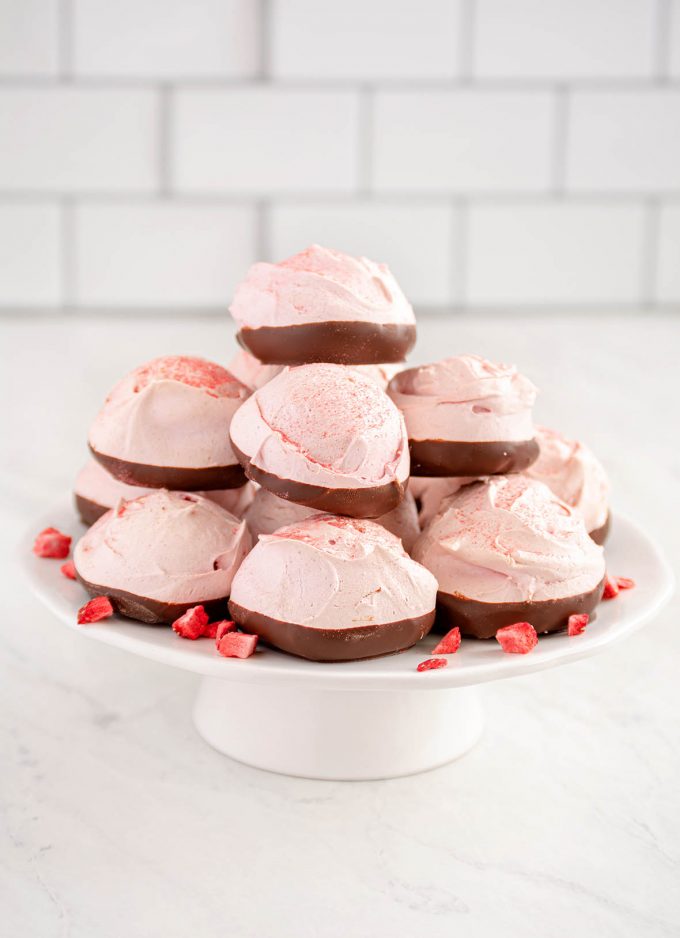 round pink meringue cookies dipped in chocolate and stacked on a small white cake pedestal. 