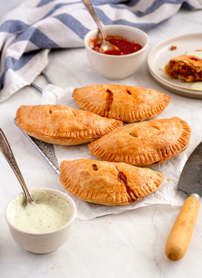 Four empanadas on a rectangle cooling rack, with two small dishes full of salsa and avocado sour cream