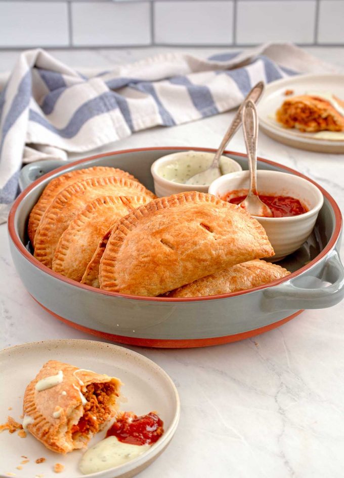 Empanadas piled in a round serving dish, with two small sauce dishes full of salsa and sour cream