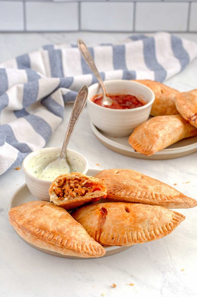 Three empanadas on a small late, one cut in half showing turkey filling, with sour cream dish and spoon.