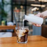 Glass filled with coffee with cream being poured over top