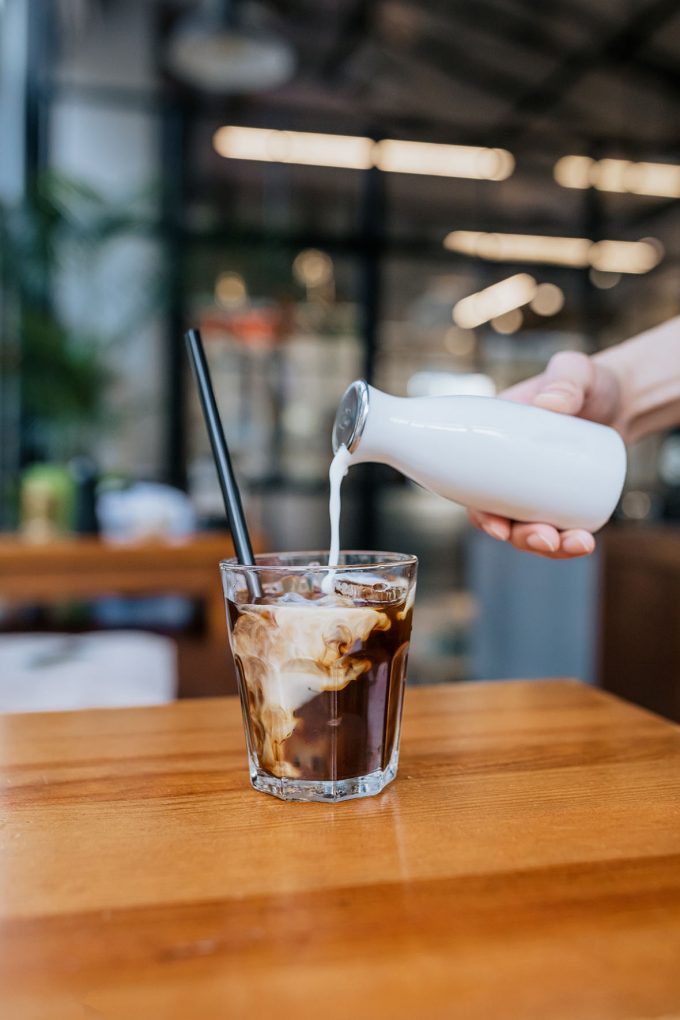 Glass filled with coffee with cream being poured over top
