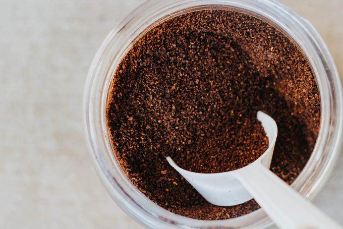 Glass jar filled with ground coffee with a white scoop digging in