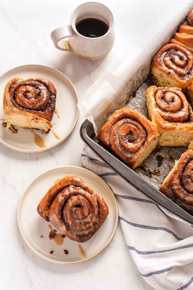 Glazed cinnamon rolls on plates with coffee in background