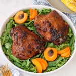 Two turkey thighs on a bed of greens, with apricot halves