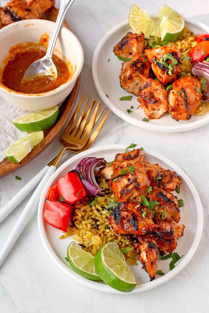 Cubes of chipotle and mango marinated grilled turkey on a small white plate, with rice, grilled onions and peppers and two lime wedges.