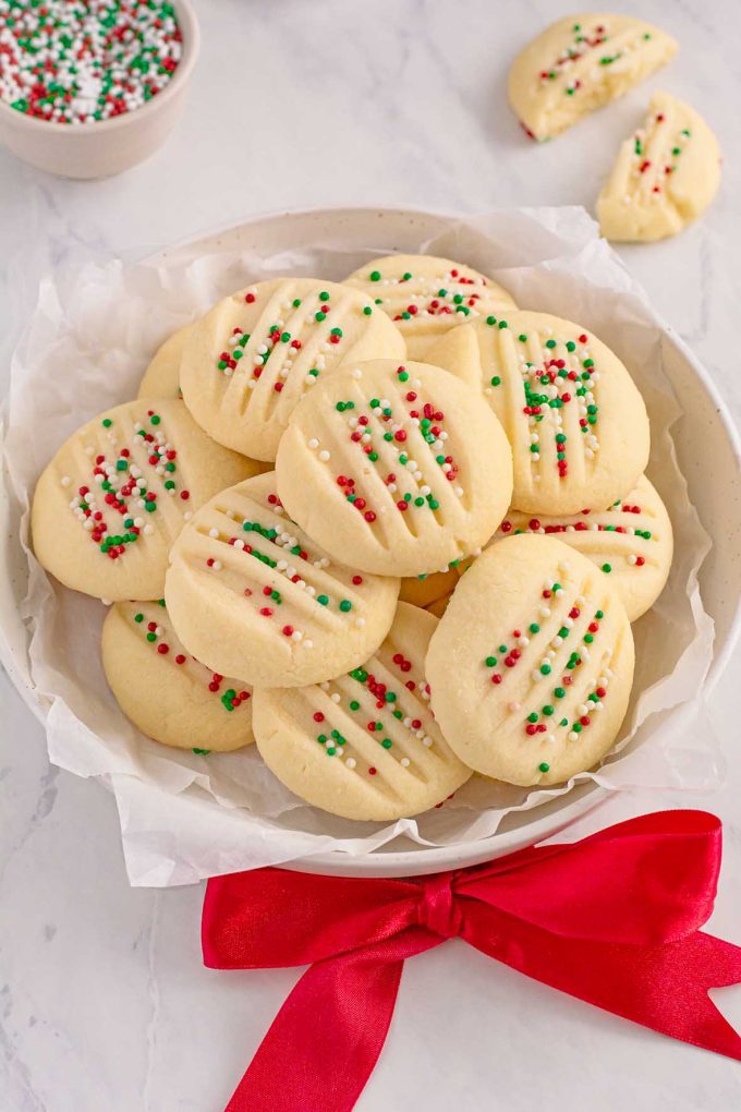 Round plate full of shortbread cookies. The cookies are topped with red, white and green sprinkles.