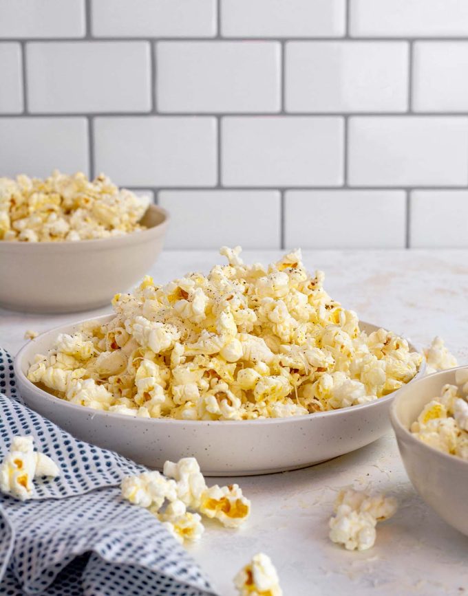 medium bowl of popcorn with grated parmesan and black pepper on top. Small bowl in background full of popcorn.