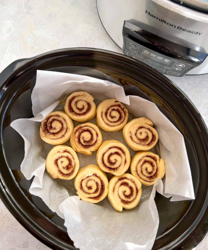 ten cinnamon rolls placed inside an oval shaped slow cooker lined with parchment paper.