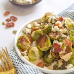 Small plate piled with roasted Brussels sprouts that were topped with pumpkin seeds, bacon pieces and crumbled feta. Drizzled with a tahini sauce.