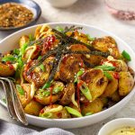 Bowl of roasted Togarashi potatoes topped with sriracha, green onions and strips of crispy seaweed.