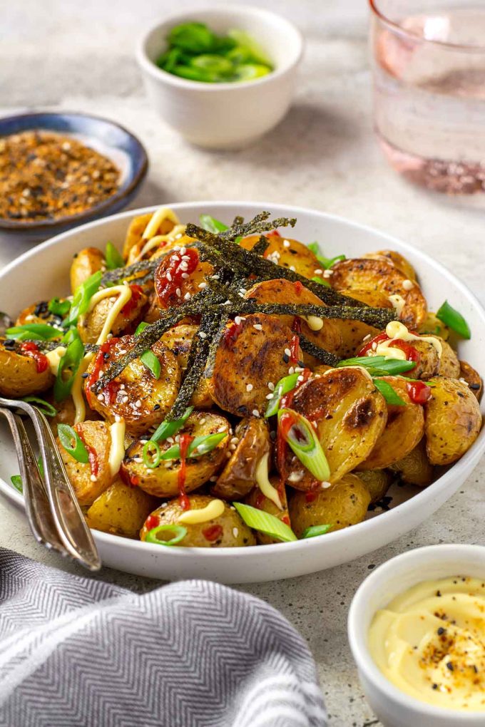 Bowl of roasted Togarashi potatoes topped with sriracha, green onions and strips of crispy seaweed.