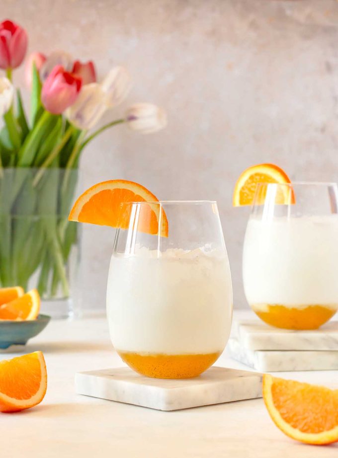 Two cocktail glassed sitting on marble coasters. pinks tulips in a vase in the background.