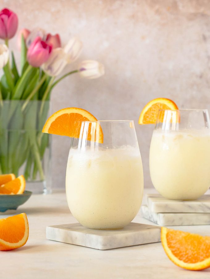 Two cocktail glasses filled with orange creamsicle beverage. Orange slices wedged on the rims of each cup.