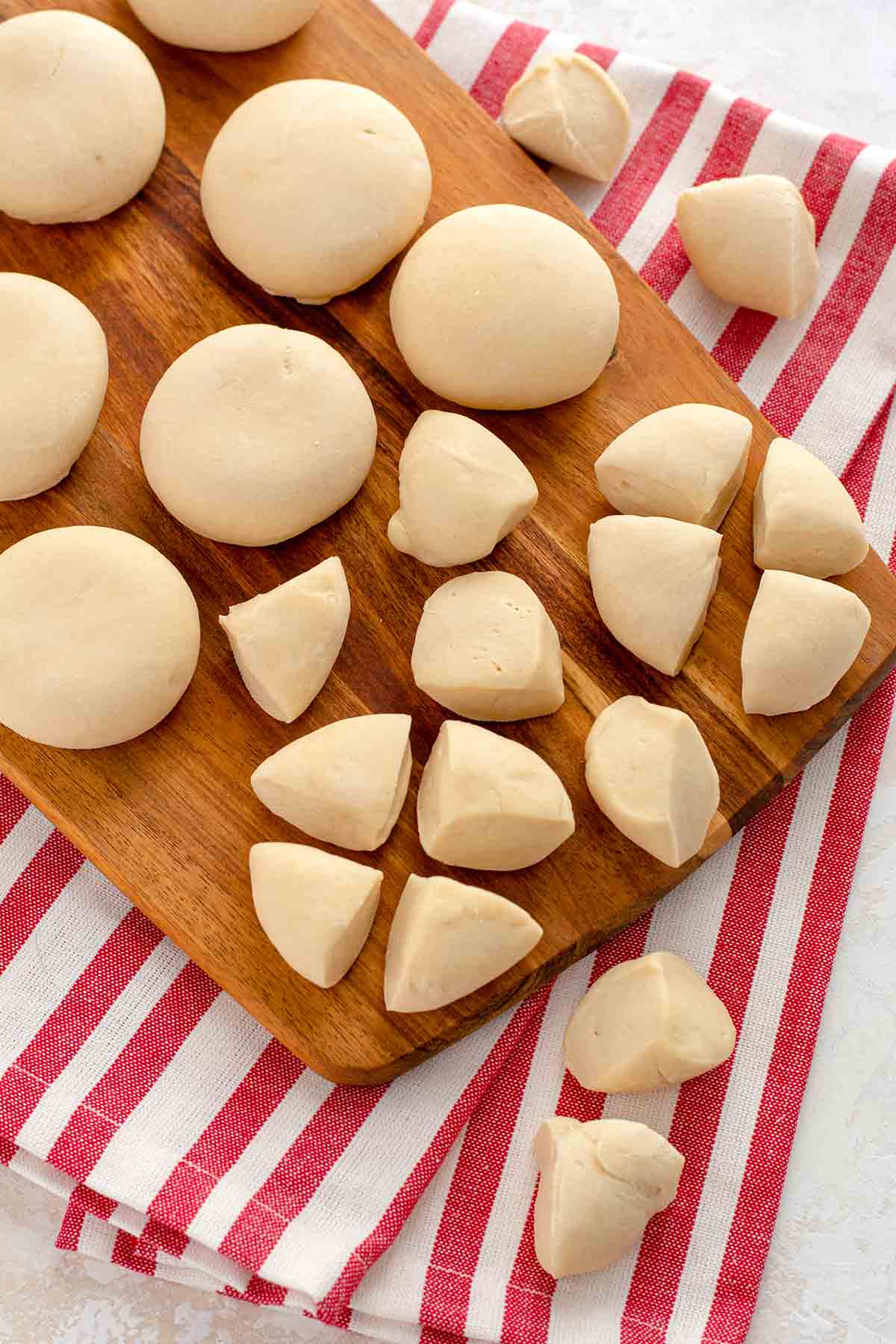 Frozen dinner rolls, cut into quarters on a wooden cutting board.