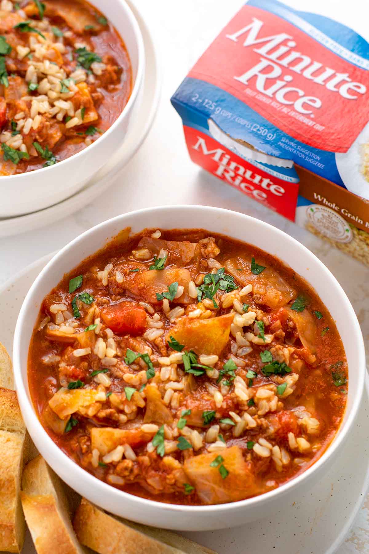 Close up of the bowl of cabbage roll soup to show rice, tomatoes and cabbage. Sprinkle of parsley onto. Minute Rice packaging in the top right corner.