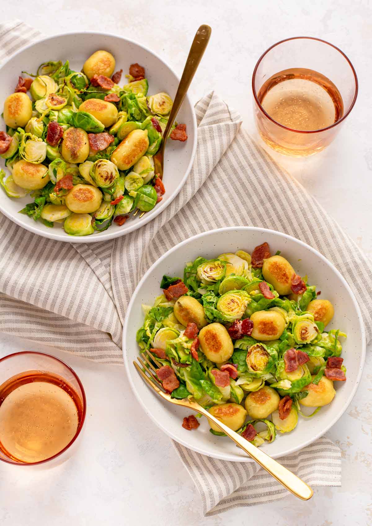 Overhead shot of two plates of sautéed Brussels sprouts and crispy gnocchi and bacon. Two small cups of ginger ale beside the plates.